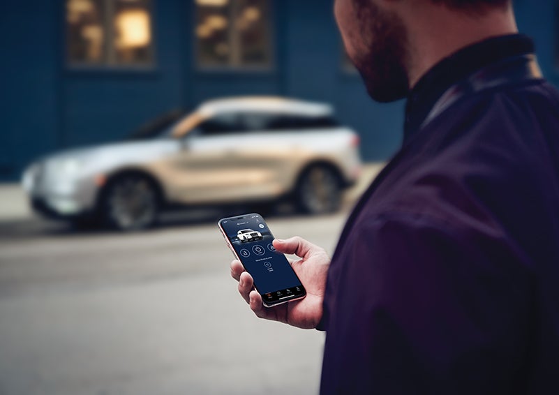 A person is shown interacting with a smartphone to connect to a Lincoln vehicle across the street. | Midland Lincoln in Midland MI