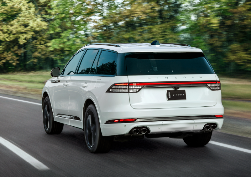 A white 2025 Lincoln Aviator® SUV is being driven away down a road lined with colorful trees. | Midland Lincoln in Midland MI