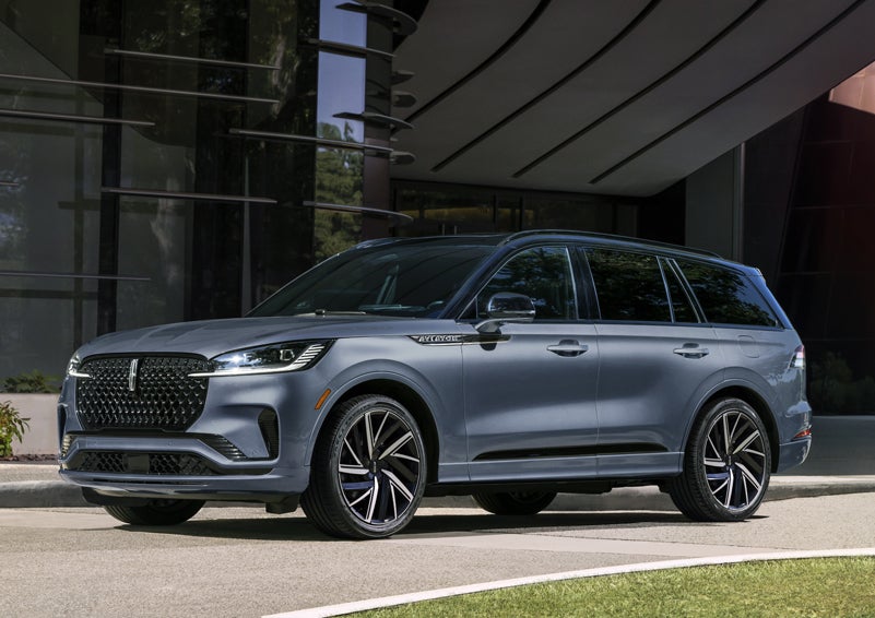A gray 2025 Lincoln Aviator® SUV is parked outside a modern building showcasing the driver’s side of the vehicle. | Midland Lincoln in Midland MI