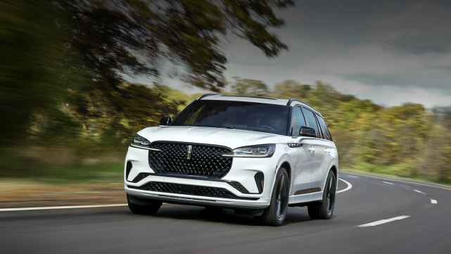 A white 2025 Lincoln Aviator® SUV is being driven down a road lined with trees. | Midland Lincoln in Midland MI