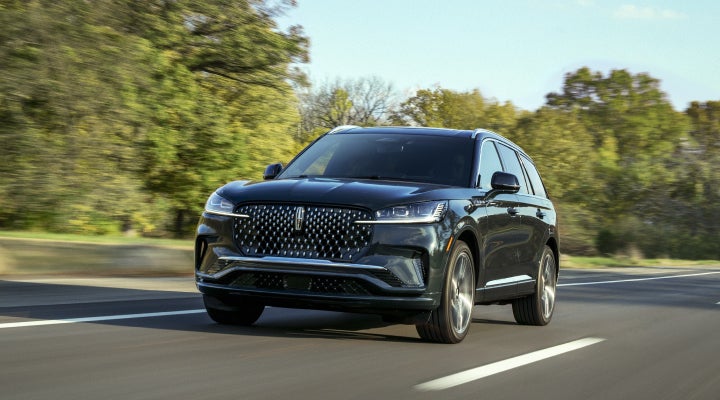 A 2026 Lincoln Black Label™ Aviator® SUV is being driven down a road lined with trees. | Midland Lincoln in Midland MI