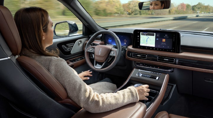 A 2027 Lincoln Aviator® SUV is being driven hands-free on a highway lined with trees. | Midland Lincoln in Midland MI