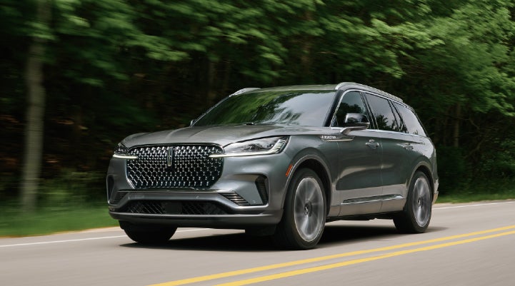 A 2027 Lincoln Aviator® SUV is being driven down a road lined with trees. | Midland Lincoln in Midland MI