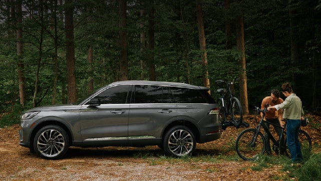 A father and son load e-bikes on a bike rack attached to a 2027 Lincoln Aviator® SUV. | Midland Lincoln in Midland MI
