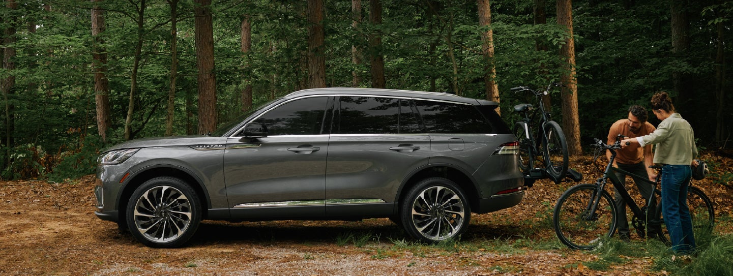 A father and son load e-bikes on a bike rack attached to a 2027 Lincoln Aviator® SUV. | Midland Lincoln in Midland MI